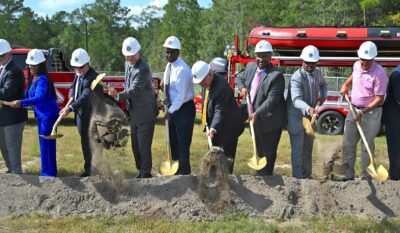 A line of people use shovels to dig a patch of dirt in a ceremonial groundbreaking.