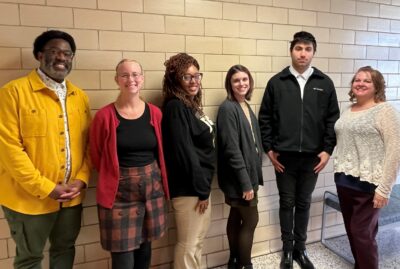 A group of five people, smiling at the camera, stand against a tile wall.