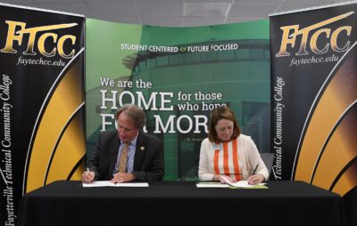 Mark Sorrells and Amanda Lee each sign paperwork while sitting at a table.