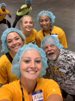 A group of young woman and one coach, most of them wearing hair nets, pose for a selfie.