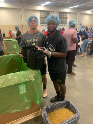 Two students pose for a photo next to a box of meals.