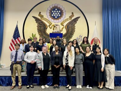 A group of American and Japanese college students and faculty stand in front of the US Seal.