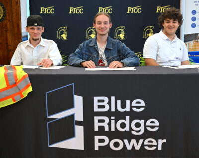 Three students sit at a table with a tablecloth that says Blue Ridge Power.