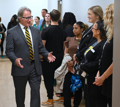 A man in a suit talks with people in a hallway.