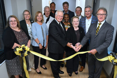 A group of people stand behind a ribbon ready to cut it.