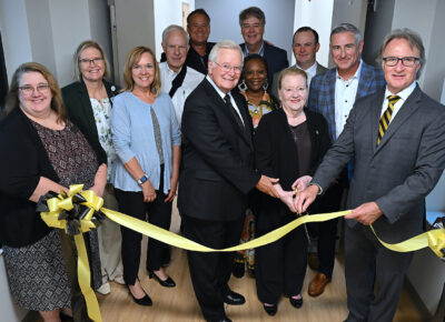 A group of people stand behind a ribbon ready to cut it.