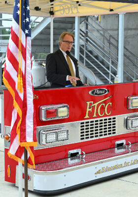 A man in a suit speaks at a podium designed to look like the front of a fire truck.