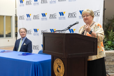 A woman speaks at a podium while a man looks on.