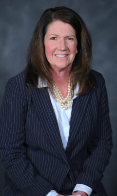 Susan Evans seated wearing a dark suit, light dress shirt, and a pearl necklace.