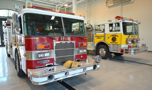 Two fire trucks - one fire and one yellow - sit in the bay at the Fire & Rescue Training Center.