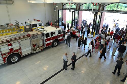 Crowd photo of people in the garage bay. Two fire trucks are visible on the left side of the photo.