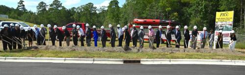 A wide photo of a row of people use shovels to perform a ceremonial groundbreaking.